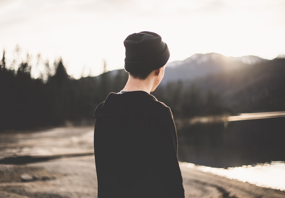 A person with their back to the camera looking toward a lake